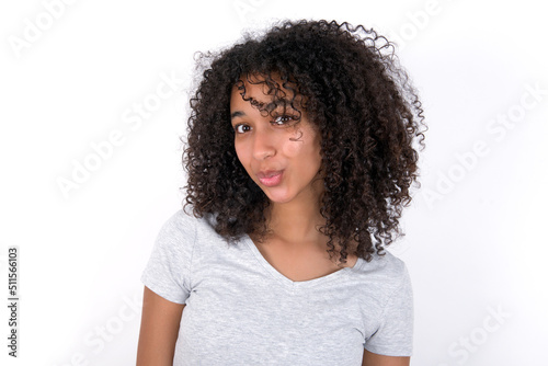 Shocked Young beautiful girl with afro hairstyle wearing grey t-shirt over white wall look empty space with open mouth screaming: Oh My God! I can't believe this. © Roquillo