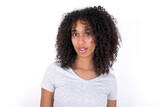 Shocked Young beautiful girl with afro hairstyle wearing gray t-shirt over white background stares bugged eyes keeps mouth opened has surprised expression. Omg concept