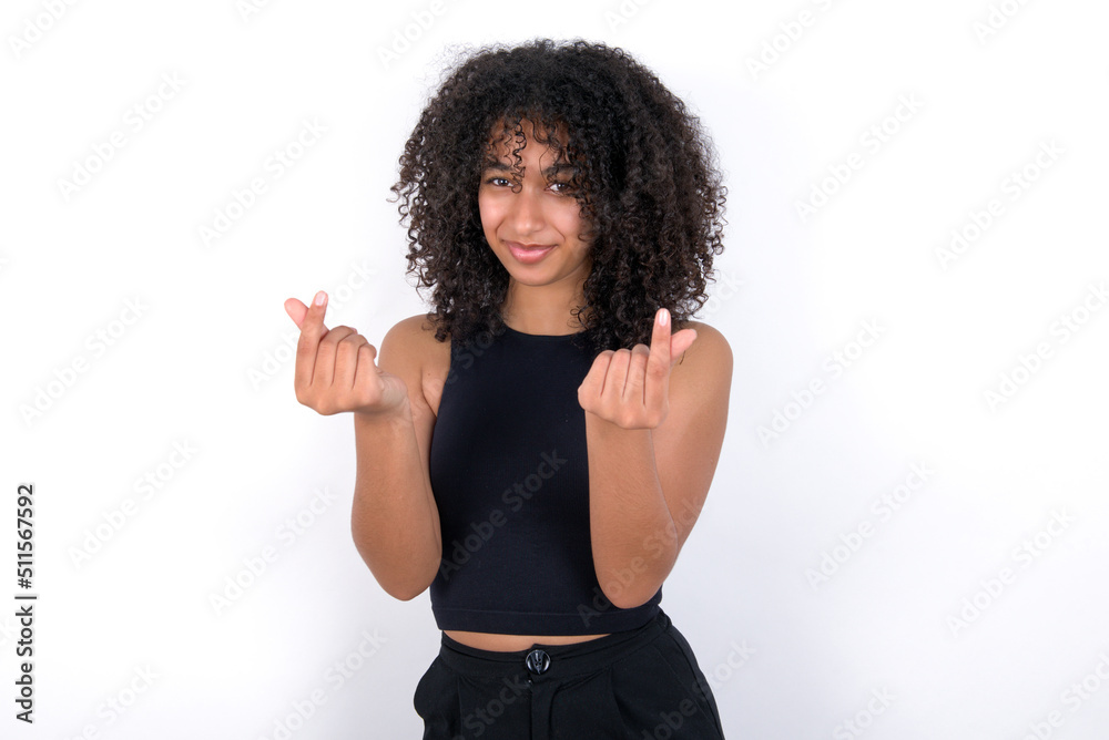 Young beautiful girl with afro hairstyle wearing black tank top over white background doing money gesture with hands, asking for salary payment, millionaire business Young beautiful girl with afro hairstyle wearing black tank top over white background doing money gesture with hands, asking for salary payment, millionaire business