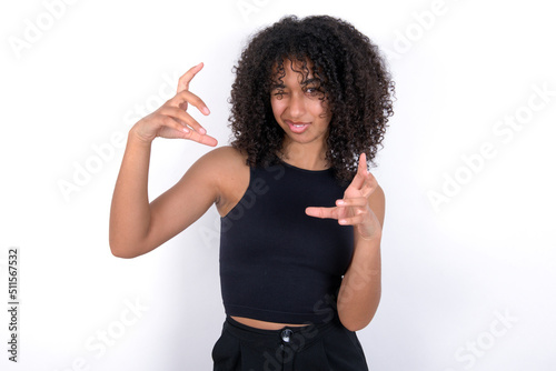 Young beautiful girl with afro hairstyle wearing black tank top over white background Shouting frustrated with rage, hands trying to strangle, yelling mad.