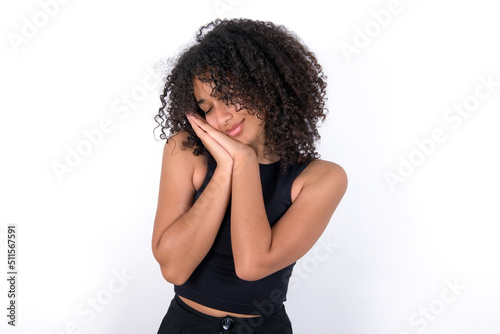 Young beautiful girl with afro hairstyle wearing black tank top over white background sleeping tired dreaming and posing with hands together while smiling with closed eyes.