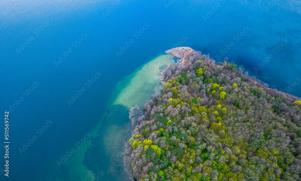 Top down view of the island in the lake. Blue water and mixed trees.