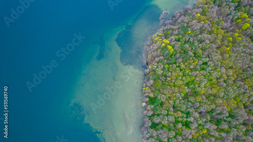 Top down view of the island in the lake. Blue water and mixed trees. © Jakub Łukasik