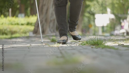 Woman with blindness disability walking on sidewalk contain tactile paving guide blocks using long white cane or blind cane a mobility tool to detect objects in the path for vision impairment people. photo