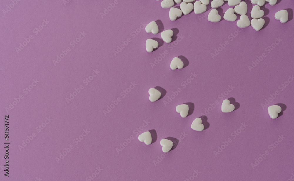 Top view of spilled heart shape white pills on purple background with copy space