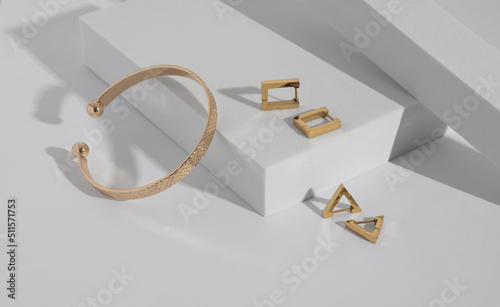 Tableau sur toile Modern gold bracelet and geometric earrings on white podium with copy space