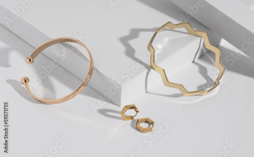 Fényképezés Two modern geometric shape golden bracelets and earrings pair on white podium wi