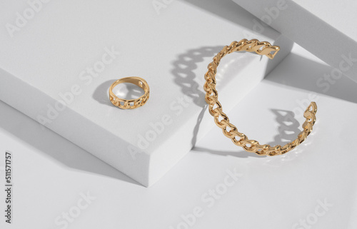 Chain shape golden modern bracelet and ring on white podium with copy space