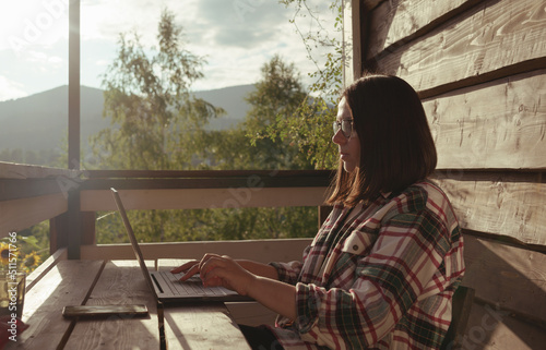 Burnette woman working on laptop outdoors in sunny summer day photo