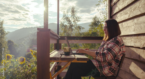 Woman working outdoor on terrace in sunny day in wooden cabin in the mountains of Ukraine