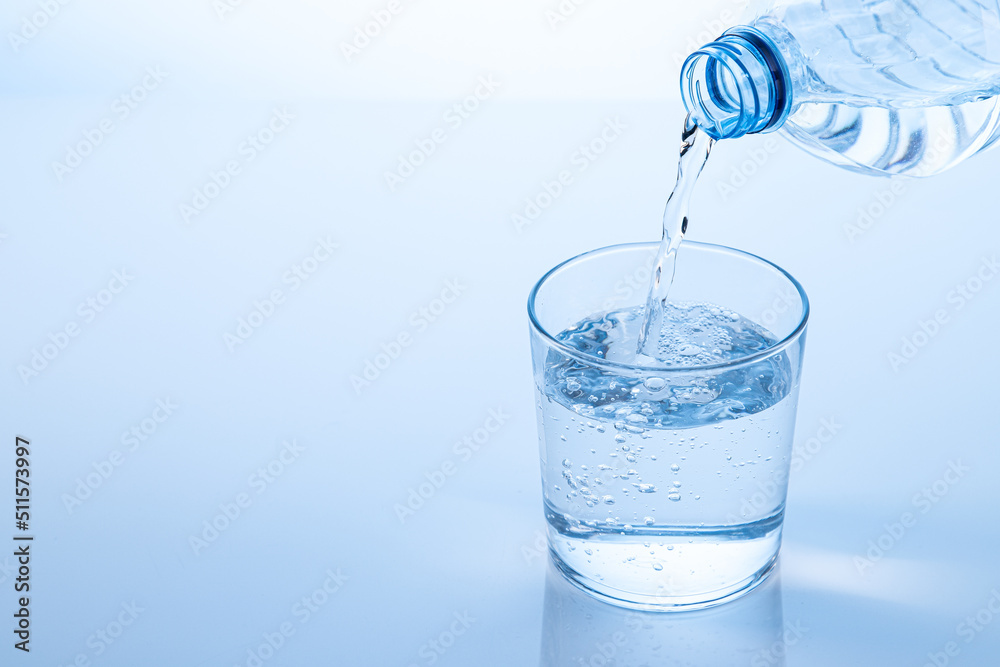 Pouring water from the bottle in to the glass isolated on blue background with copy space. Pouring water from the bottle in to the glass isolated on blue background with copy space.