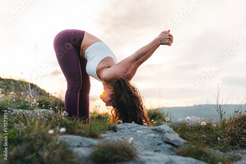 Fit young female doing Prasarita Padottanasana C pose during yoga session at sundown photo