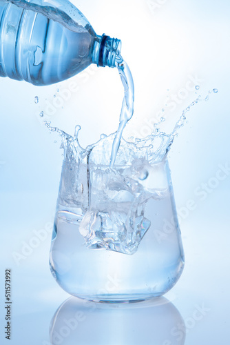 Pouring mineral water and splashing from bottle into glass on blue background. Vertical format.