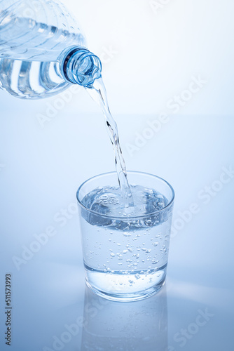 Pouring water from the bottle in to the glass isolated on blue background. Vertical format.