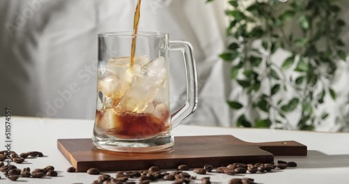 4k video, pouring brewing coffee into glass full of ice. Making cold coffee drink in slow motion. Cold Brew black coffee  with coffee beans.