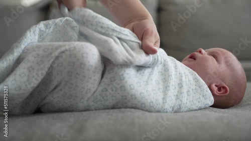 Close up of newborn baby being swaddled in a blanket in home by mother photo