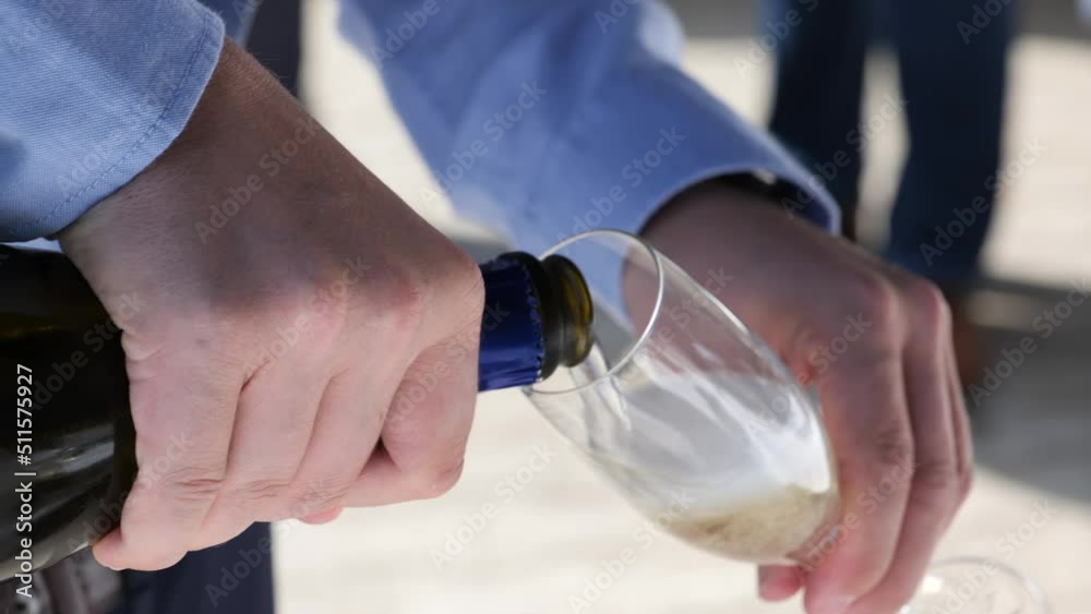 Close up of slowly pouring champagne from a bottle into a glass at a garden party or wedding party. Bubbles of champagne rising in the glass. Close up of slowly pouring champagne from a bottle into a glass at a garden party or wedding party. Bubbles of champagne rising in the glass.