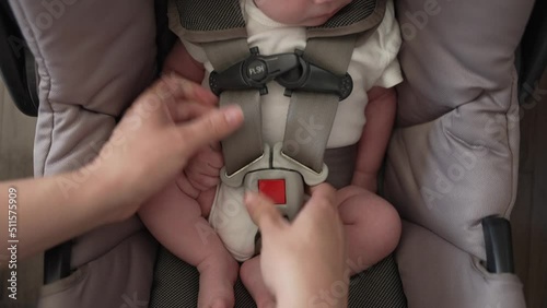 Close up mother's hands buckle safety straps of 5 point harness infant car seat