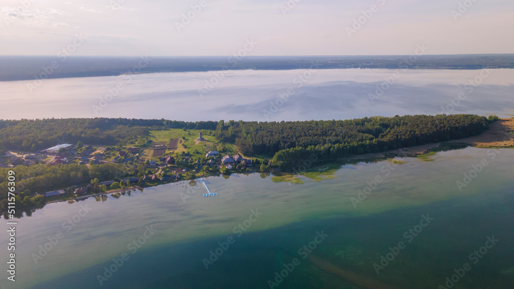 Aerial view of lake and small village on the peninsula. Sunset evening light by calm water on warm beautiful summer day.