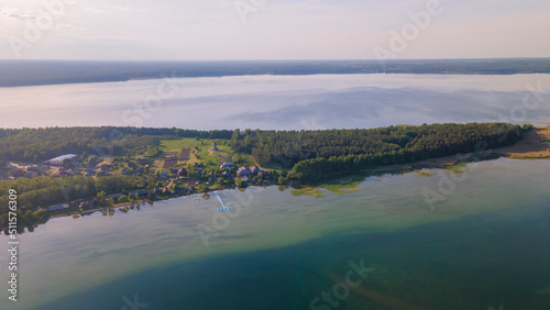 Aerial view of lake and small village on the peninsula. Sunset evening light by calm water on warm beautiful summer day.