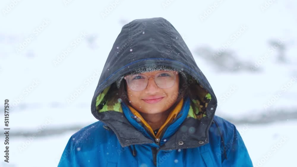 Close up portrait of happy Indian girl standing in snowfall and smiling at camera while hiking on mountain during snowfall at Manali in Himachal Pradesh, India. Winter holidays and adventure concept Close up portrait of happy Indian girl standing in snowfall and smiling at camera while hiking on mountain during snowfall at Manali in Himachal Pradesh, India. Winter holidays and adventure concept