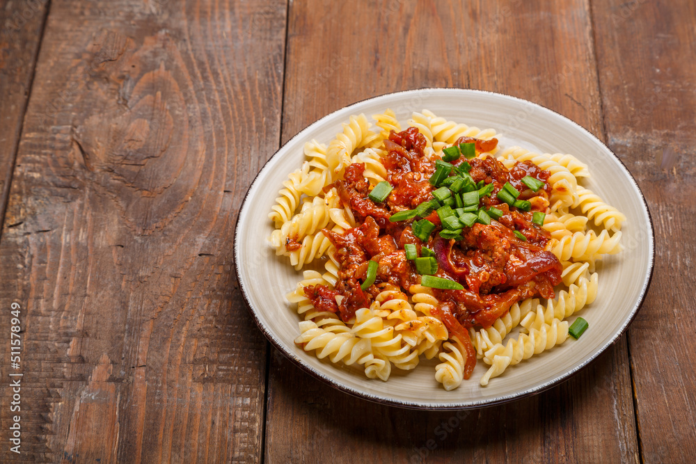 Beige plate with bolognese pasta on a wooden table sprinkled with green onions. Beige plate with bolognese pasta on a wooden table sprinkled with green onions.
