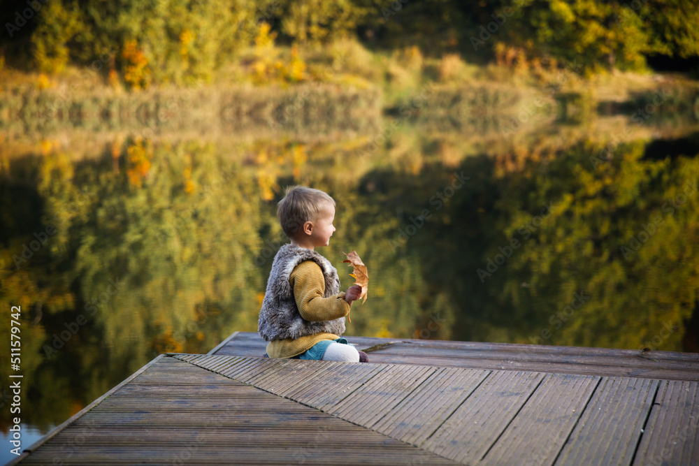 Fototapeta premium Cute European bald toddler baby in park in fall near lake