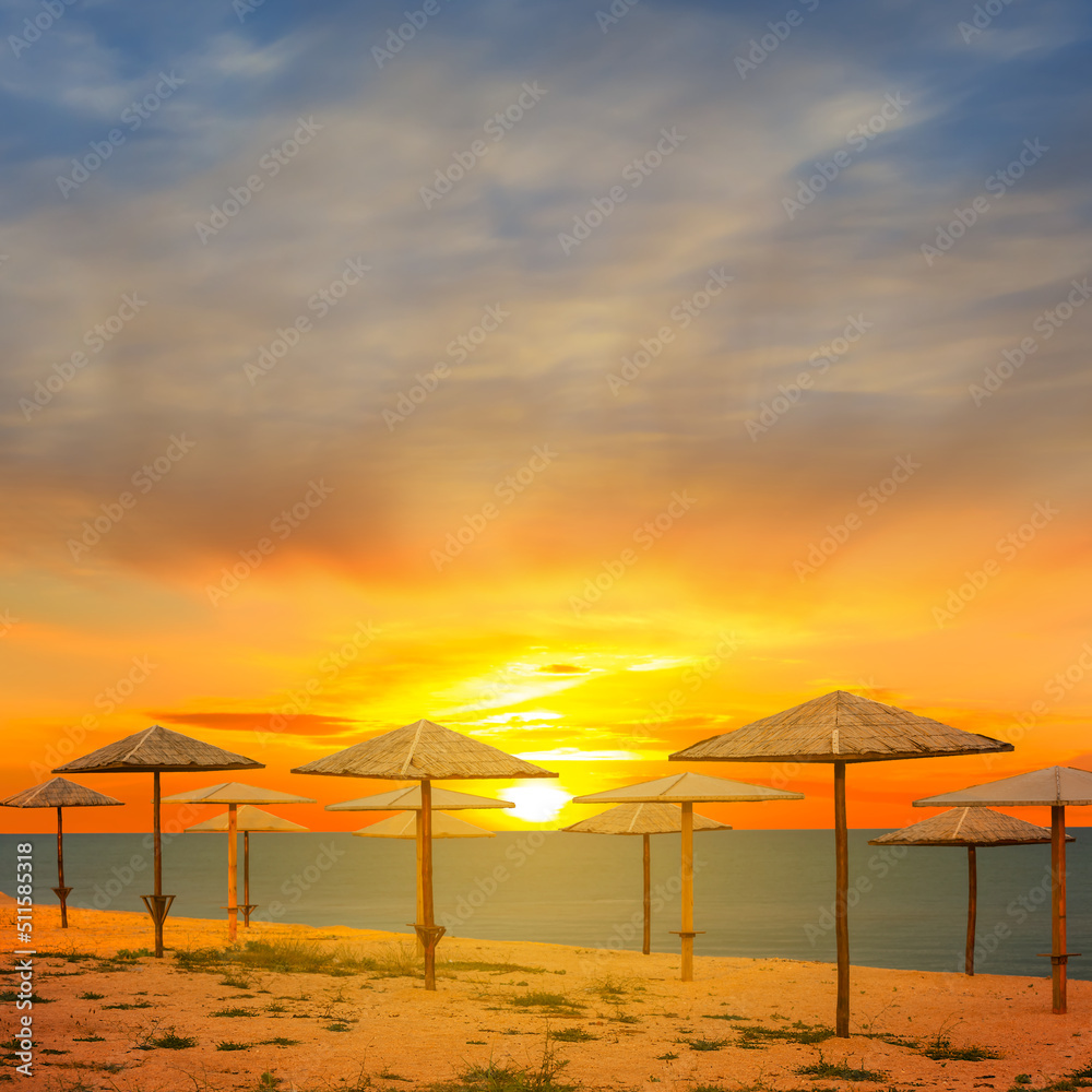 sandy sea beach with sun umbrella at the sunset