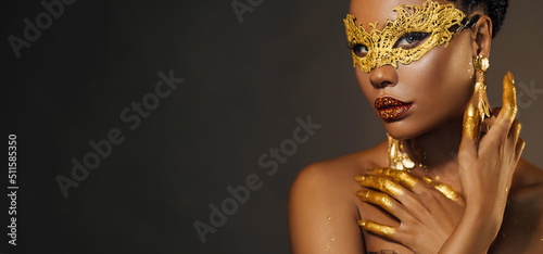 Portrait sexy african woman face close up in golden venetian carnival mask. Girl fashion model perfect skin, golden evening holiday makeup, glitter diamond stones lip gloss, hands in gold liquid paint