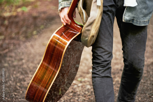 Modern traveling minstrel. A cropped closeup shot of a young man carrying a guitar while walking down a forest path.