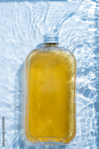 A plastic drink cold clear bottle is placed in the water pool. Transparent blue colored clear water surface texture with ripples, splashes and bubbles nature background Water waves in sunlight