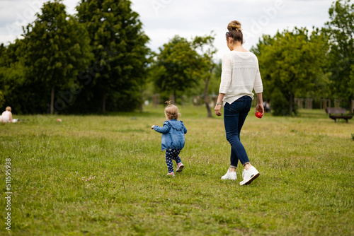 mother and daughter outdoors, having fun in park, toddler is running on the grass