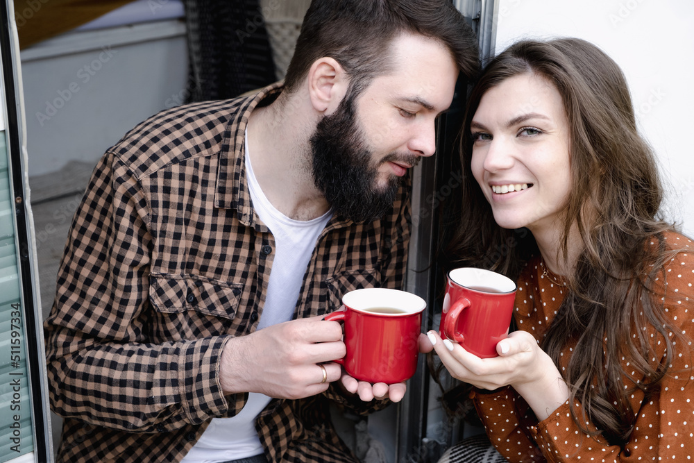 Young caucasian couple is traveling in travel van. Romantic atmosphere of relaxation. Road trip around country for the weekend. Man and woman sitting in camper and drinking tea. Millennial generation Young caucasian couple is traveling in travel van. Romantic atmosphere of relaxation. Road trip around country for the weekend. Man and woman sitting in camper and drinking tea. Millennial generation
