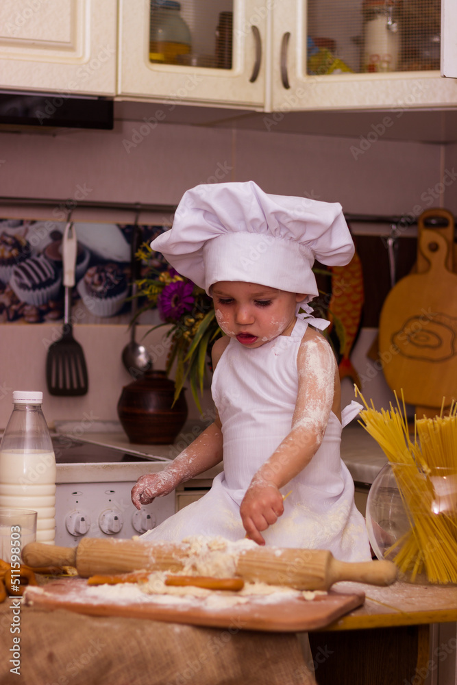 A little boy in cook's clothes rolls out dough with a rolling pin A little boy in cook's clothes rolls out dough with a rolling pin