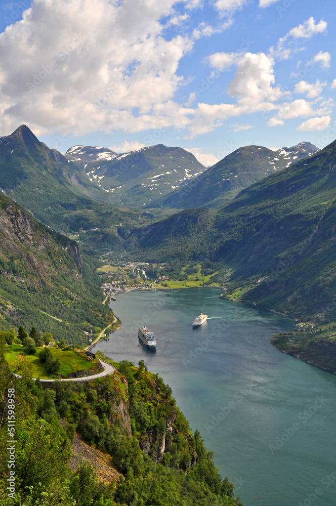 A deep fjord in the village of Geiranger in Norway. Boats are parked at sea, behind them are a few houses and high mountains rise at the top.