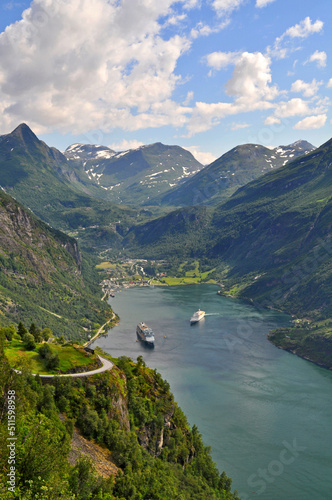 A deep fjord in the village of Geiranger in Norway. Boats are parked at sea, behind them are a few houses and high mountains rise at the top. © Jan