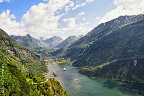 A deep fjord in the village of Geiranger in Norway. Boats are parked at sea, behind them are a few houses and high mountains rise at the top.