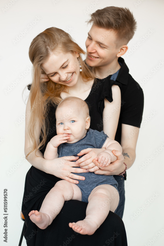 Happy mom and dad embrace and hold baby in dark clothes, laugh and rejoice on white background. Cute relationship between parents and infant child, free copy space. Happiness and love in family Happy mom and dad embrace and hold baby in dark clothes, laugh and rejoice on white background. Cute relationship between parents and infant child, free copy space. Happiness and love in family