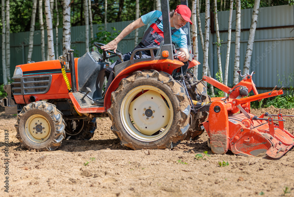 A farmer on a mini tractor loosens the soil for the lawn. Land cultivation, surface leveling. A farmer on a mini tractor loosens the soil for the lawn. Land cultivation, surface leveling.