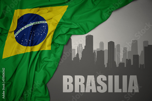 abstract silhouette of the city with text Brasilia near waving national flag of brazil on a gray background.