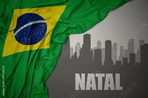 abstract silhouette of the city with text Natal near waving national flag of brazil on a gray background.
