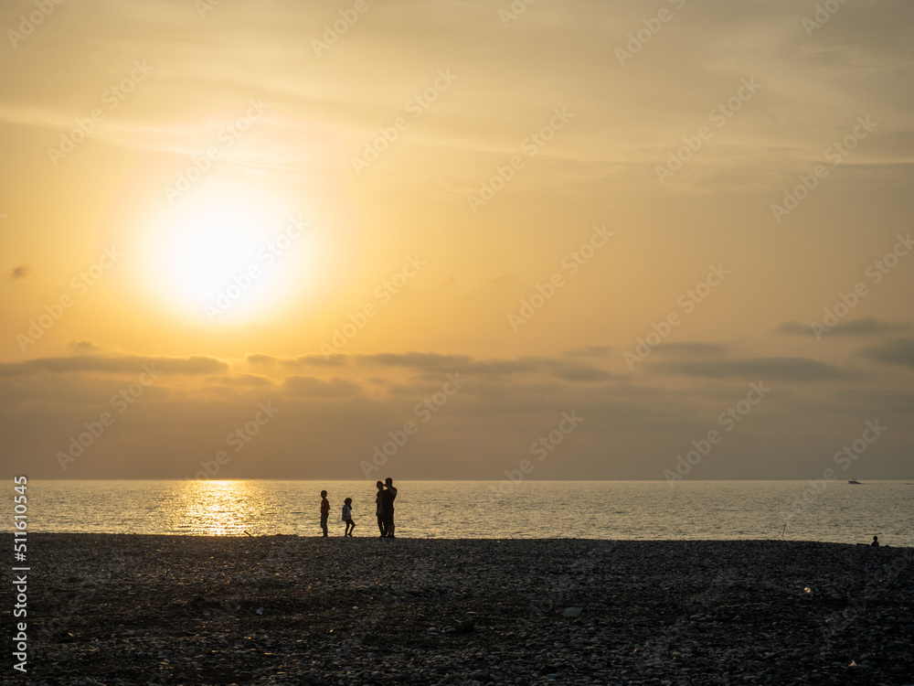 Silhouettes of people against the backdrop of a bright sunset. Orange sunset. Family on vacation.  Sea
