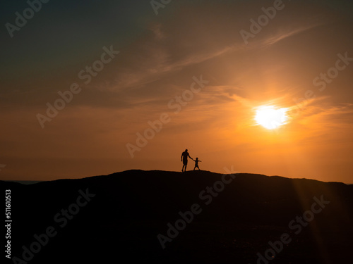 The boy leads his father through the hills towards the sun. Beautiful sunset Silhouette