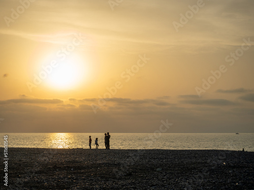 Silhouettes of people against the backdrop of a bright sunset. Orange sunset. Family on vacation. Sea