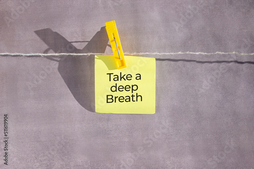 Take a deep breath text on a yellow sticker on a rope with clothespins on a grey background.