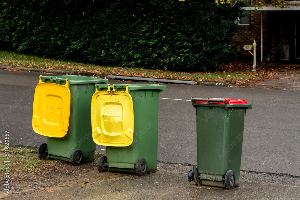 Australian garbage wheelie bins with colourful lids for recycling and general household waste lined up on the street for council rubbish collection Australian garbage wheelie bins with colourful lids for recycling and general household waste lined up on the street for council rubbish collection