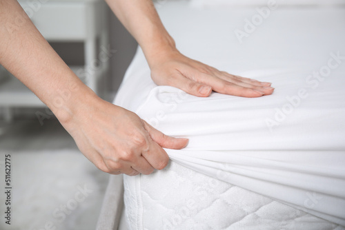 Fotografie Woman putting white fitted sheet over mattress on bed indoors, closeup