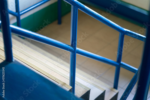 Close-up at stairway with blue metal handrail. Building interior part photo, selective focus.