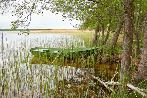 Small green boat anchored in forest lake. Scandinavia. Transportation, traditional craft, recreation, leisure activity, healthy lifestyle, local tourism, sport, rowing, hiking, summer vacations themes photo