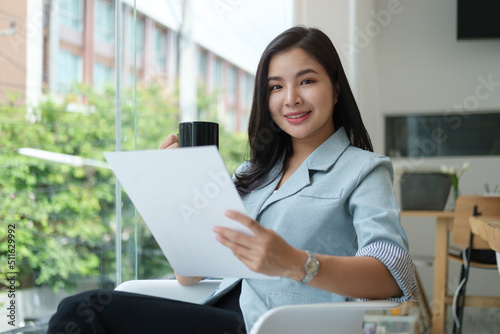 Smiling asian businesswoman sitting in bright modern office and reading document.